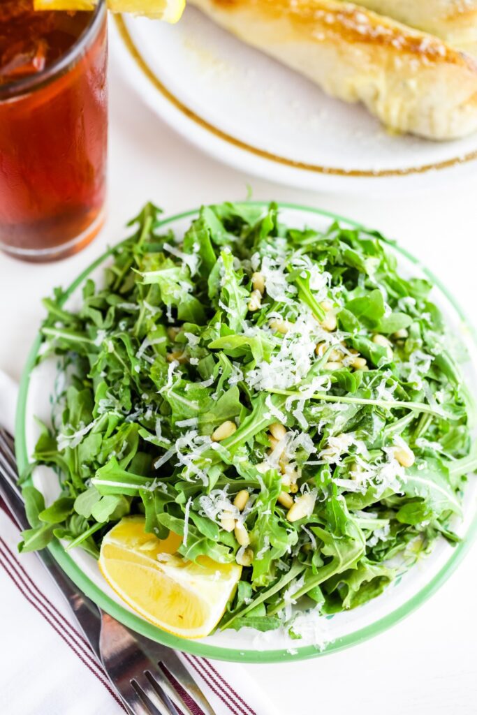 Giada Candied Lemon and Arugula Salad served with a drink and breadsticks.