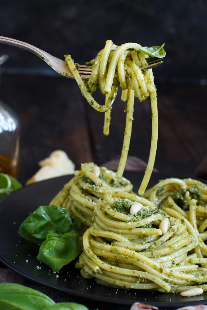 Spaghetti with basil pesto on a black plate, garnished with fresh basil leaves and pine nuts.