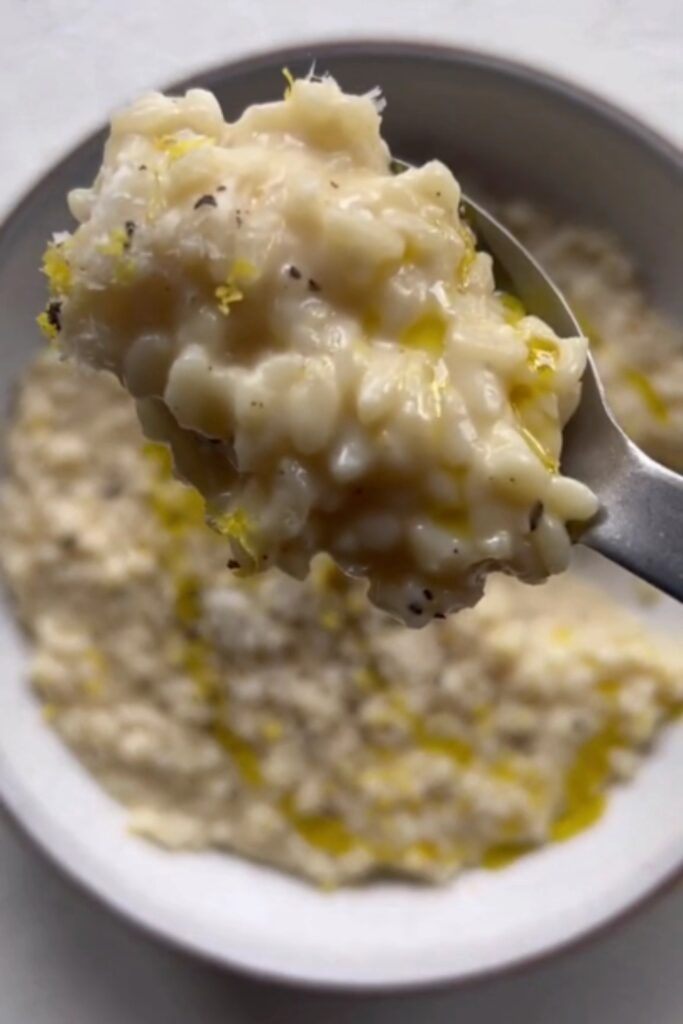 A spoonful of Giada De Laurentiis Basic Risotto with Parmesan and black pepper, lifted above a bowl.